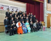 31人のスーツや振袖を着た新成人が舞台前で4段に並んで集合写真を撮っている様子
